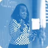 blue tinted image of a person speaking in front of a chalkboard
