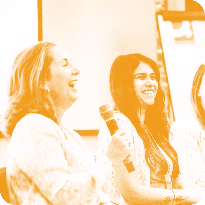 two people laughing while one holds a microphone